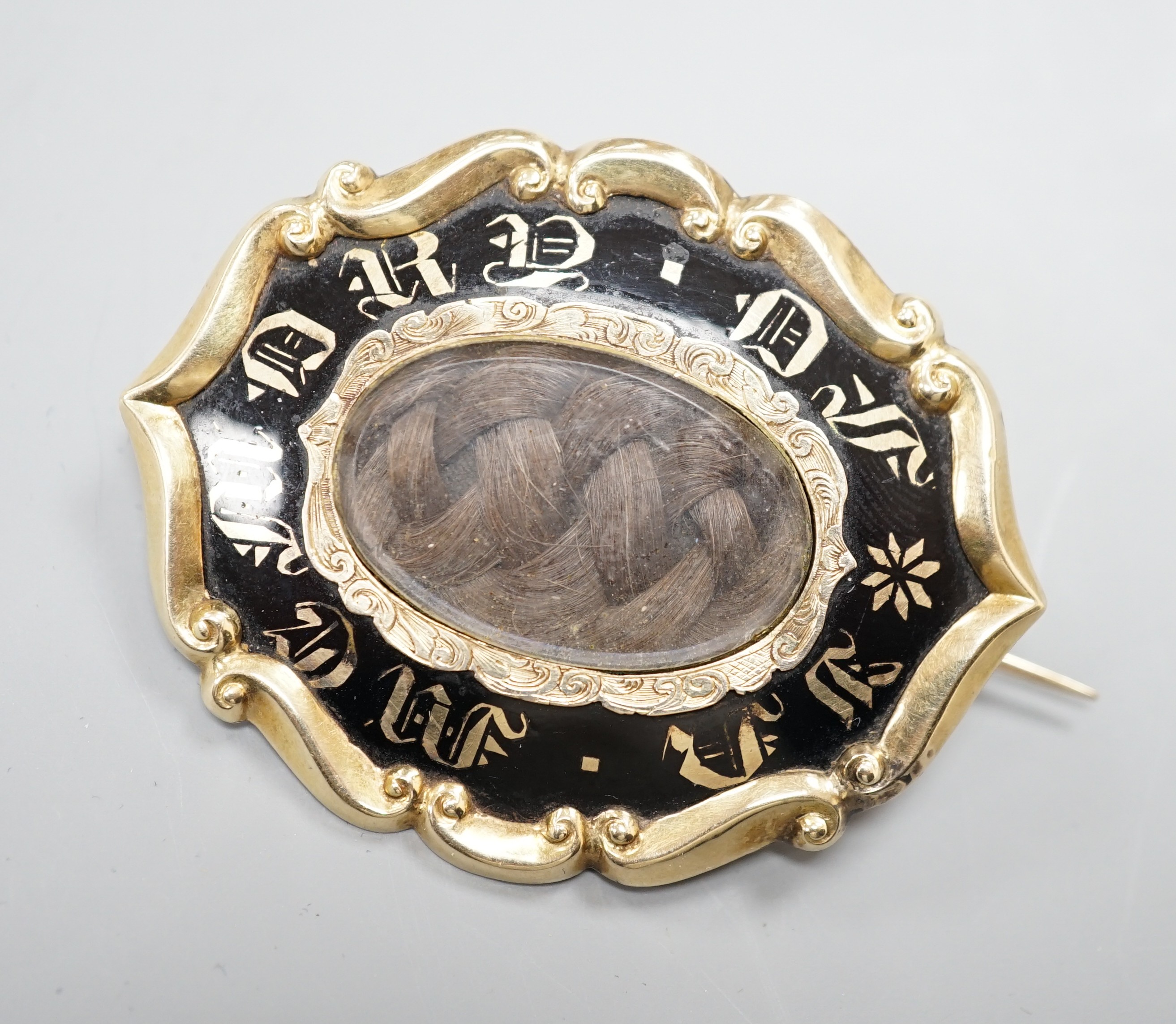 A Victorian yellow metal overlaid and black enamel 'In Memory Of' shaped oval brooch, with central glazed plaited hair panel, 52mm.